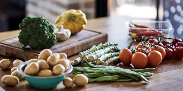 Fresh living and fresh eating. A wooden kitchen surface displaying a chopping board and various vegetables like tomatoes, baby potatoes and asparagus. 